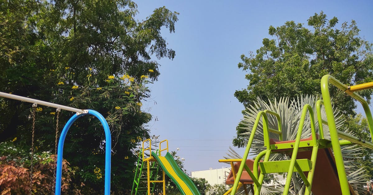 Colorful playground equipment in Yeola, India, surrounded by lush trees under a clear blue sky.